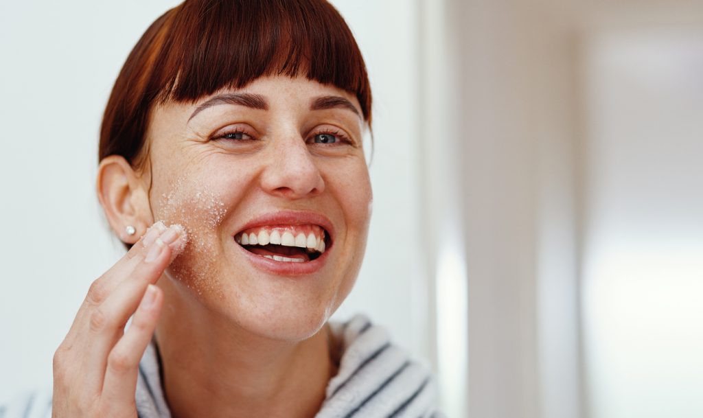 young woman smiling while applying natural sea salt as a skin renewal facial